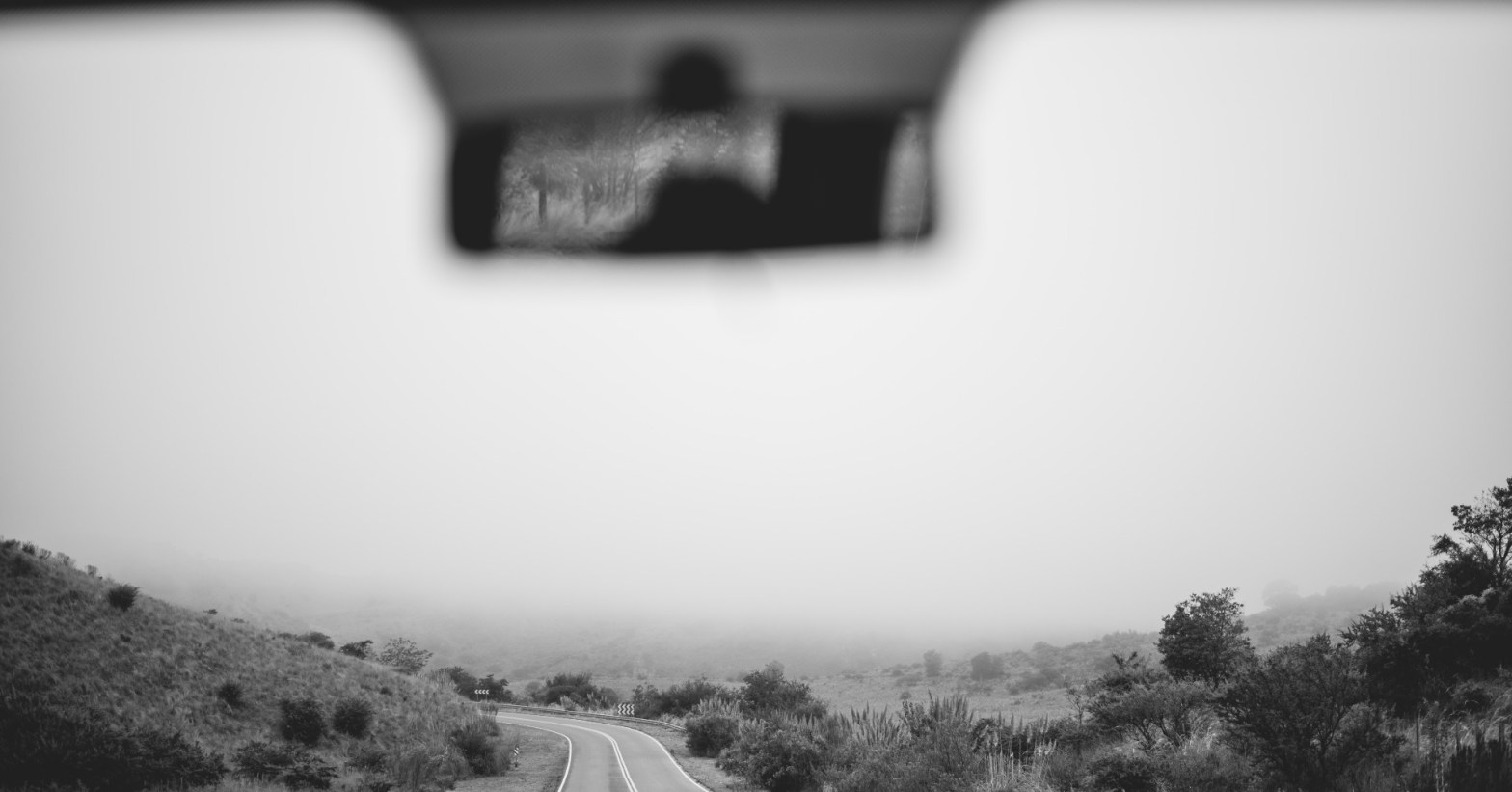 Photo of of a car windshield showing a winding road ahead and the rearview mirror