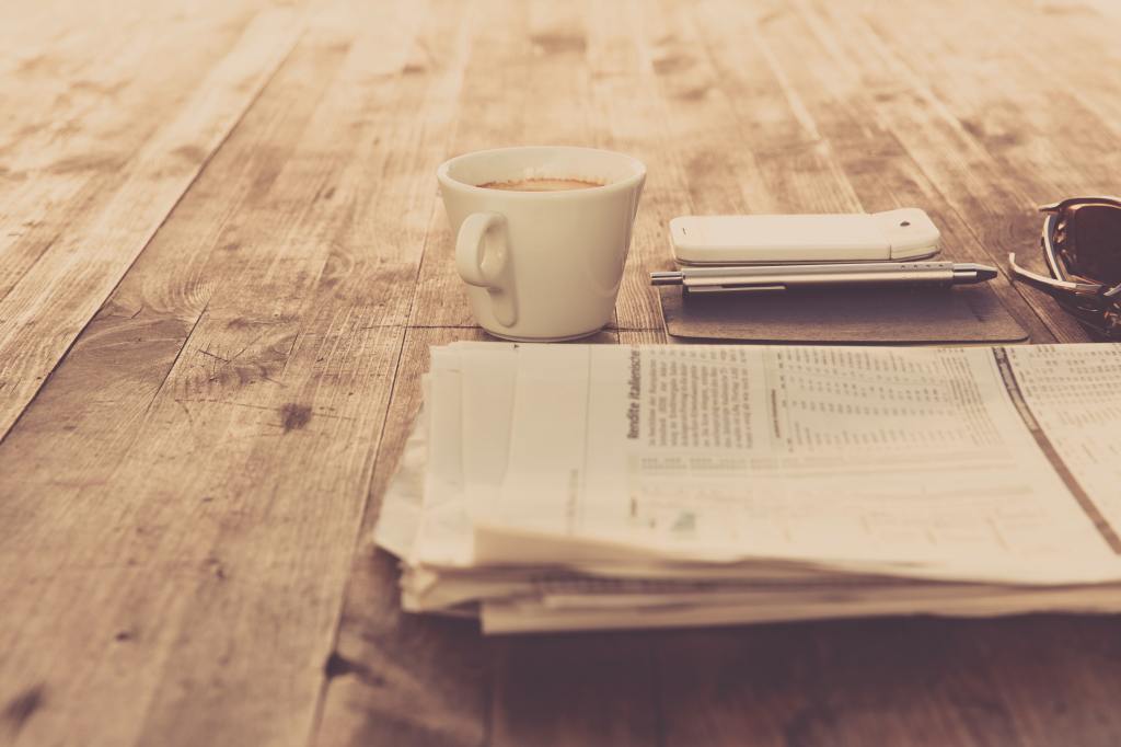 A cup of coffee, papers and a pen and planner laid out on a wooden table.