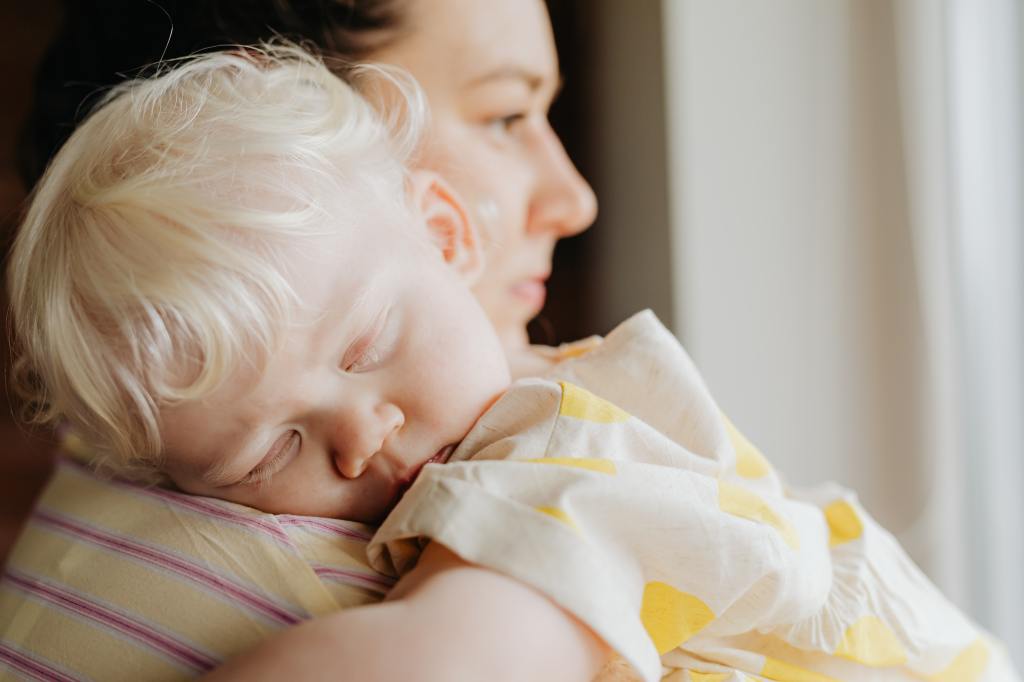 A baby sleeps on her moms shoulder while being held.